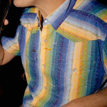 Man wearing The Gris Gris colorful striped outdoor shirt while drinking a dark beverage