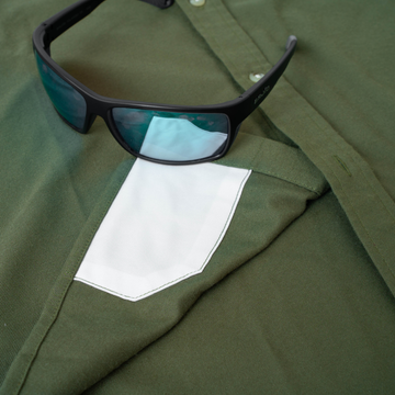 Close-up of The Roosevelt green outdoor shirt with black sunglasses resting on the pocket