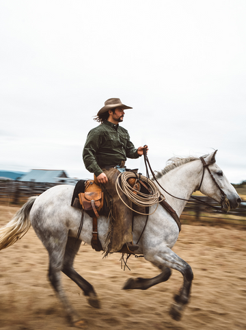 Man wearing a green shirt and hat riding a white horse outdoors