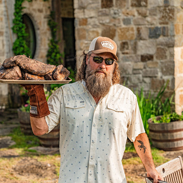 Man wearing The Llano shirt outdoors holding a plate of smoked meat with barbecue glove