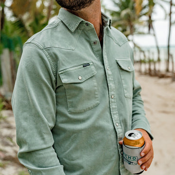 man holding beverage wearing green pearl snap denim shirt