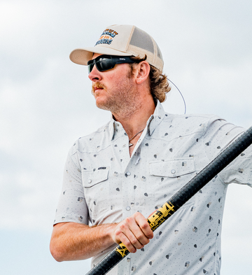 Man wearing patterned outdoor shirt and cap holding a paddle against cloudy sky