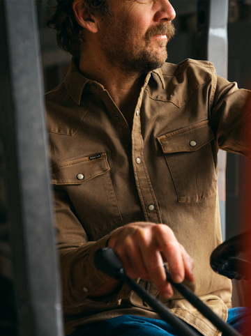 Man wearing a brown button-up shirt with flap pockets operating machinery controls