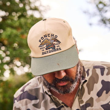 Man wearing Eagle and Trout Hat with beige crown and green brim outdoors