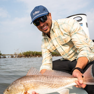 Man wearing The Encinitas shirt holding a large fish on a boat outdoors