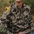 Man wearing The Entre Rio camouflage shirt sitting outdoors among greenery and holding an object
