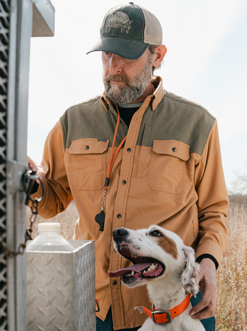 Man in an outdoors shirt and cap with a white and brown dog wearing an orange collar