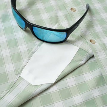 The Sapelo green plaid outdoor shirt with blue reflective sunglasses resting on it