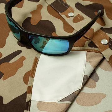 Black sunglasses with blue lenses resting on camo shirt pocket from The White Wing collection