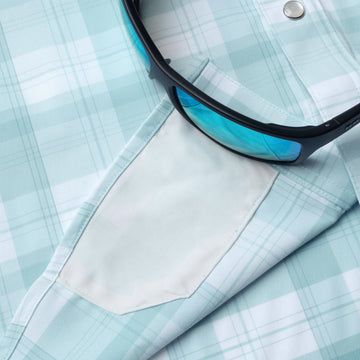 Close-up of light blue plaid shirt sleeve pocket with sunglasses resting on The Billings shirt