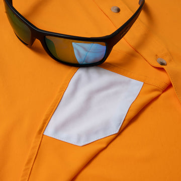 Close-up of The First and Goal shirt pocket in bright orange with reflective detail and sunglasses resting on top