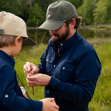 Man attaching an artificial worm to a hook while wearing the green Mallard Rope Hat