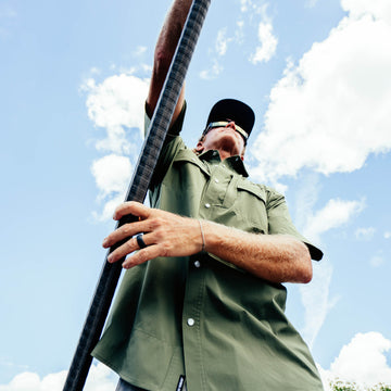 Man wearing green short-sleeve shirt holding paddle under blue sky