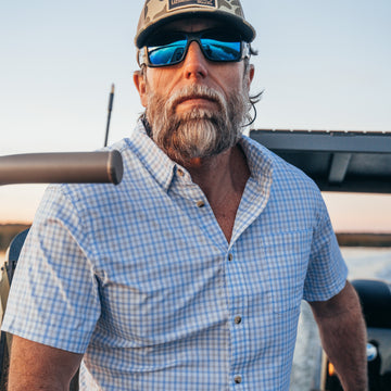 man driving boat in blue and grey plaid short sleeve