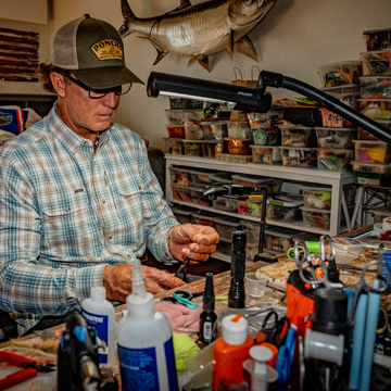 Man Tying a fly while wearing the moss agave trucker hat