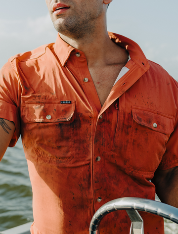 Man wearing a dirty orange shirt with boat steering wheel visible in background