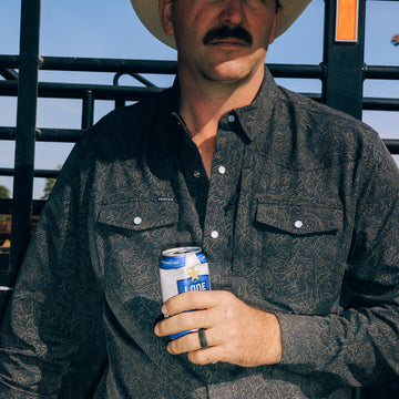 Man wearing The Pat Garrett dark patterned outdoor shirt and cowboy hat holding a can outdoors