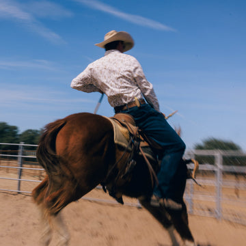 Rider wearing The Rattler shirt on bucking horse outdoors
