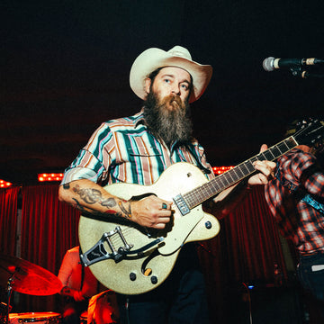 Man wearing The Frontman striped shirt and cowboy hat playing electric guitar on stage