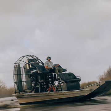 Man wearing The Chicken on a Hook shirt riding an airboat through a swamp
