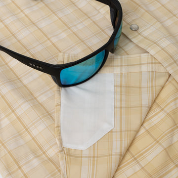 Close-up of beige plaid outdoor shirt pocket from The Sweetwater with black sunglasses resting on fabric
