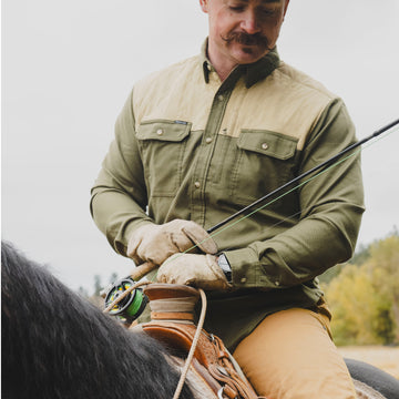Man wearing The Roosevelt outdoor shirt while riding a horse and holding fishing gear