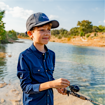 Young boy reeling in a fish wearing navy button down fishing shirt