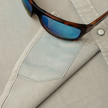 Close-up of The Stockton sunglasses with blue lenses resting on a beige outdoor shirt pocket