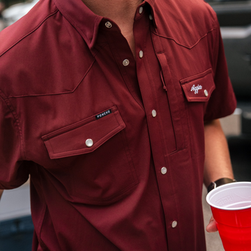 Close-up of a burgundy shirt named The Aggie with snap buttons and front pockets outdoors