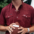Man wearing a maroon "The Aggie" shirt holding a football outdoors