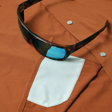 The Bertha shirt in rust with a white pocket and sunglasses resting on it