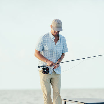 Man outdoors fishing wearing The Bow To The King shirt and beige pants