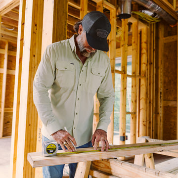 Man wearing The Carpenter shirt measuring wood at construction site