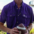 Person wearing a purple short-sleeve shirt named The Duke Dog holding a football outdoors