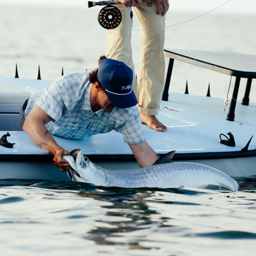 Man wearing "The End Game" shirt releasing large fish from a boat in calm water