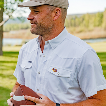 Man outdoors wearing The Eye of the Tiger white shirt holding football