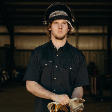 Man puts on work gloves while wearing wearing The Farrier shirt