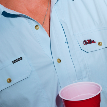 Close-up of light blue The Grove shirt with button details and red cup