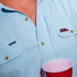 Close-up of light blue The Grove shirt with button details and red cup
