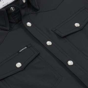 Close-up of black button-up shirt with snap buttons and flap pockets featuring The Newt label