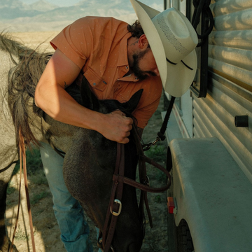 Man wearing The Joshua Tree shirt and cowboy hat hugging a horse outdoors