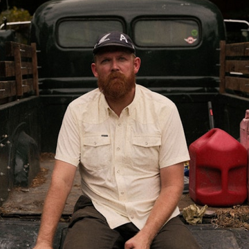 Man wearing The Medicine Bow shirt sitting on truck bed outdoors near red gas can