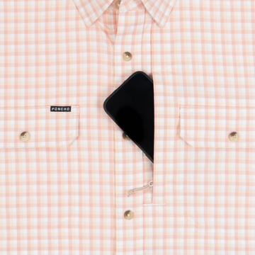 Close-up of a plaid outdoor shirt pocket featuring a secure zippered compartment holding a smartphone, highlighting The Mud Bug design.
