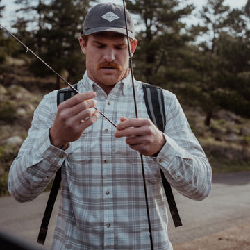 Man outdoors holding fishing rod wearing The Snowcat plaid shirt with backpack