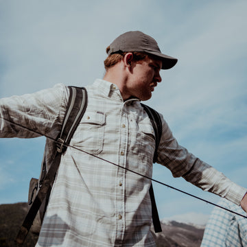 Man wearing The Snowcat shirt outdoors casting fishing line against blue sky