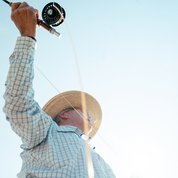 Man wearing The Soda Butte shirt casting a fishing line outdoors against a clear sky