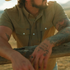 Man wearing The Sonora outdoors leaning on wooden fence with tattooed arms
