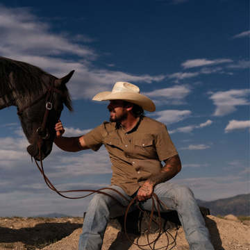 Man wearing The Sonora shirt and cowboy hat petting a horse outdoors