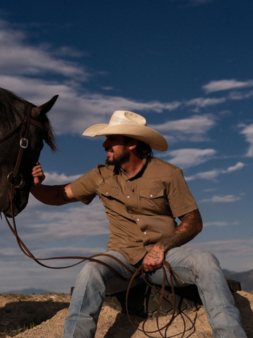Man wearing The Sonora shirt and cowboy hat petting a horse outdoors