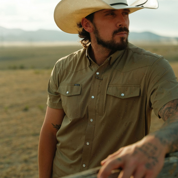Man wearing The Sonora shirt and cowboy hat outdoors in a rural landscape